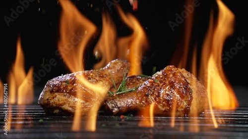 Chicken drumsticks or legs grilled on hot barbecue charcoal flaming grill with spices sprinkled on top. Juicy chicken meat roasted on bbq grill. slow motion photo