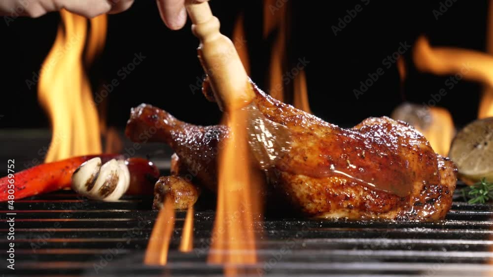 Chicken thighs grilled on hot barbecue charcoal flaming grill with sauce brushed on top. Juicy chicken meat roasted on bbq grill. slow motion