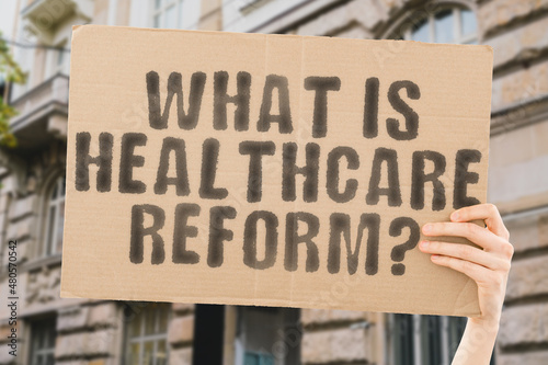The question " What Is Healthcare Reform? " on a banner in men's hand with blurred sea on the background. Improve. Renewal. Update. Campaign. Renew. Civil. Society. Community