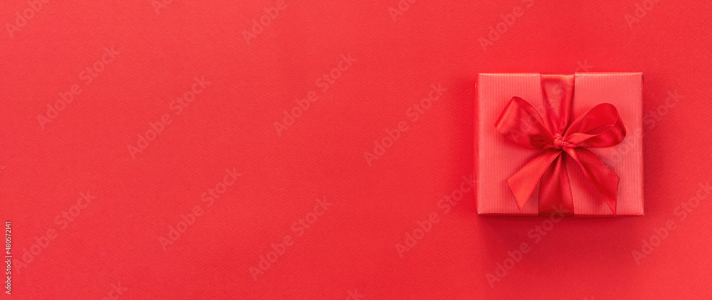 Gift box with a satin ribbon on a red background. Valentine's day promotion long banner with copy space. Valentine's day concept background for postcard, sale banner, advertising. Gift box with a satin ribbon on a red background. Valentine's day promotion long banner with copy space. Valentine's day concept background for postcard, sale banner, advertising.