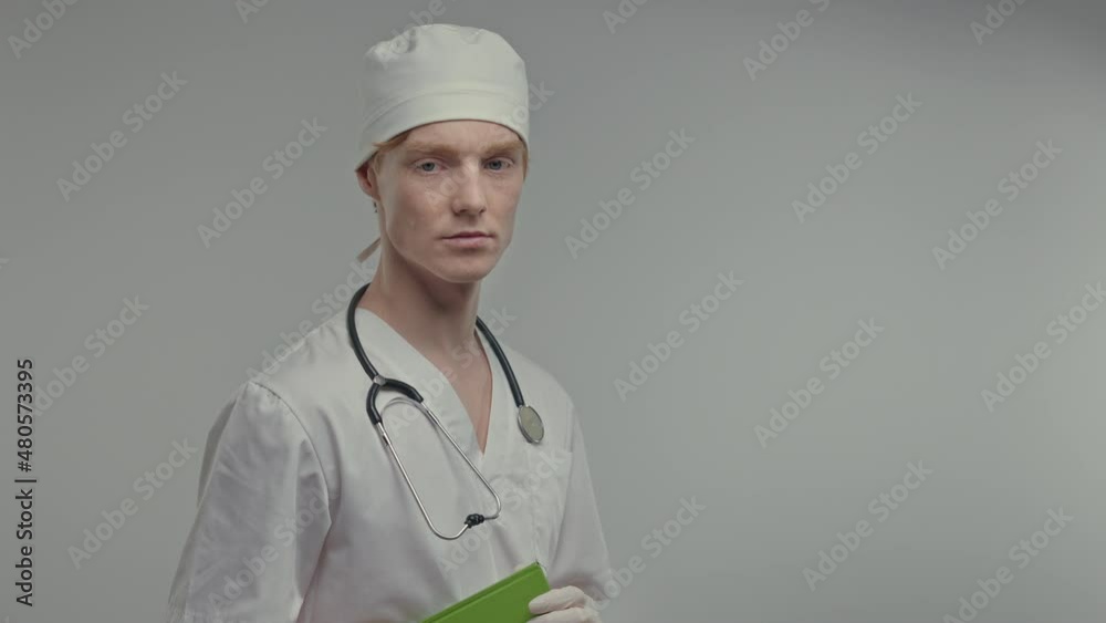 Young Doctor In Medical Gown And Gloves. He Is Holding Notebook. Young Doctor In Medical Gown And Gloves. He Is Holding Notebook.