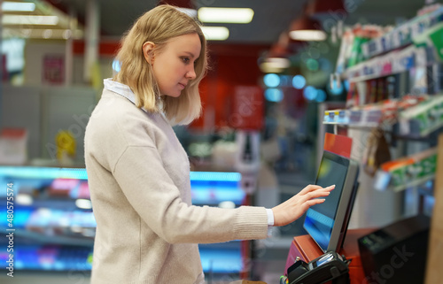 Woman pays at self-checkouts in supermarket.