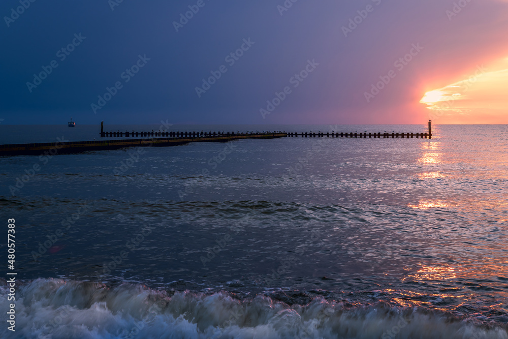 beautiful sunset and impending storm. A fishing boat and crates on the breakwater in the background