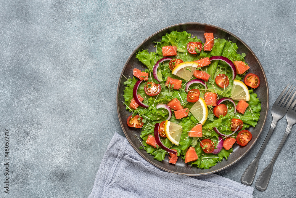 Fresh salad with salmon, tomato, lettuce leaves, microgreens, red onion and sesame seeds. Gray concrete rustic background. Top view, flat lay. Fresh salad with salmon, tomato, lettuce leaves, microgreens, red onion and sesame seeds. Gray concrete rustic background. Top view, flat lay.