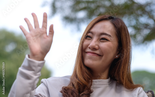 Portrait image of a young woman raising hand and say hi to friends in the outdoors