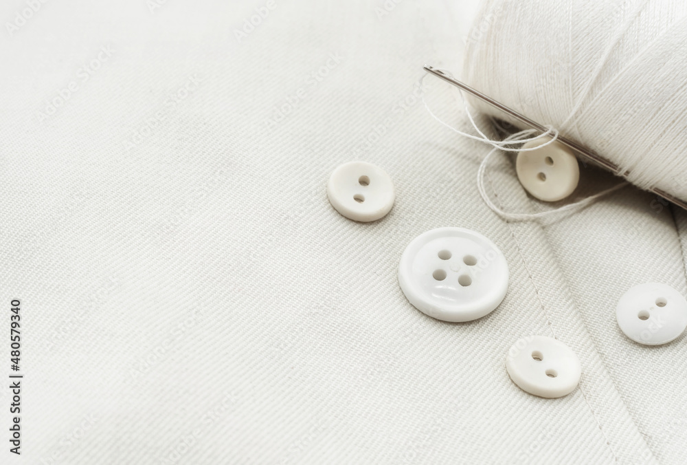 Needle with white threads, buttons on white fabric, clothes. Part of men's clothing. Needle with white threads, buttons on white fabric, clothes. Part of men's clothing.