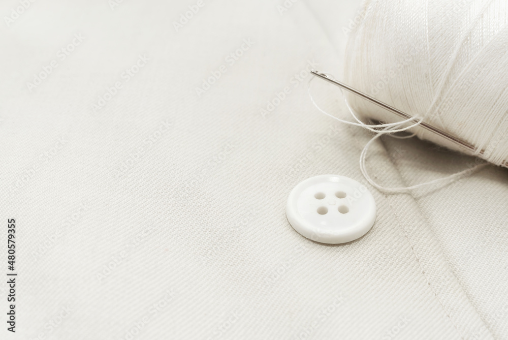 Needle with white threads, buttons on white fabric, clothes. Part of men's clothing. Needle with white threads, buttons on white fabric, clothes. Part of men's clothing.