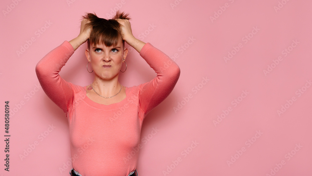 An angry, irritated young woman, isolated on a pink background, holds her head with her hands, feeling a headache.Human facial expressions, emotions. Body language. Copying space. An angry, irritated young woman, isolated on a pink background, holds her head with her hands, feeling a headache.Human facial expressions, emotions. Body language. Copying space.