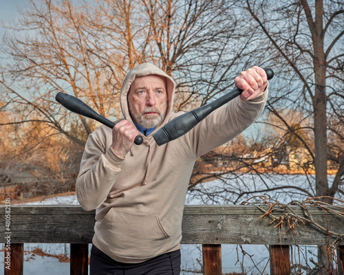 outdoor portrait of senior man (in late 60s) exercising with Indian clubs in his backyard, winter afternoon, fitness over 60 concept