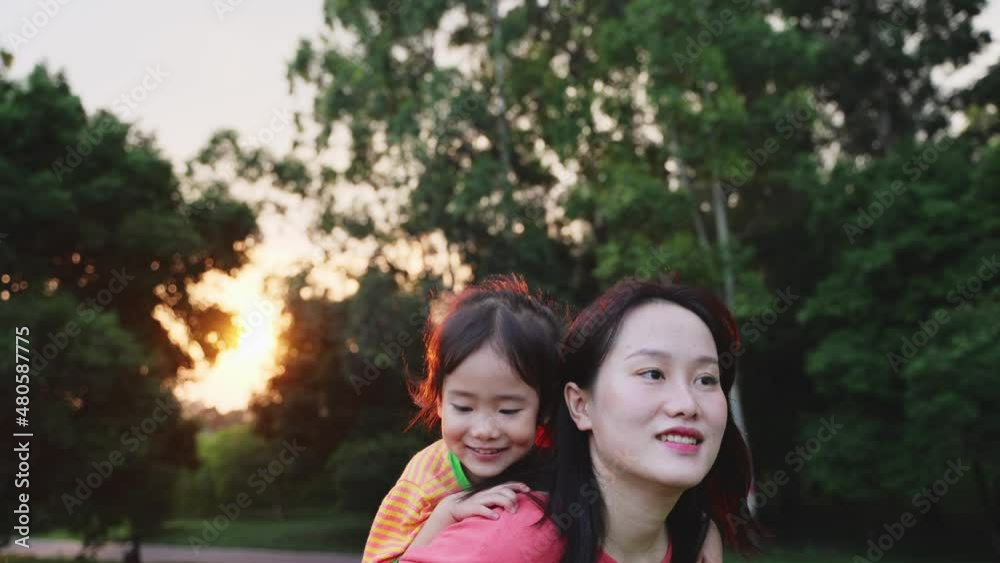 young asian woman carrying her little daughter running in the park happy child girl having fun with her mother in the park young asian woman carrying her little daughter running in the park happy child girl having fun with her mother in the park