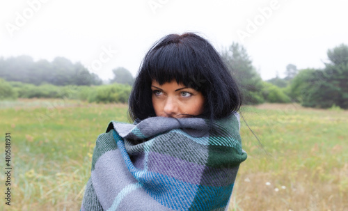 a young woman with a large scar on her face on a natural background warms herself with a woolen blanket