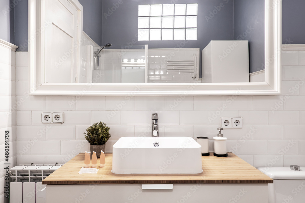 Front view of cloakroom with square porcelain sink on wood countertop and white framed mirror on white tiled wall Front view of cloakroom with square porcelain sink on wood countertop and white framed mirror on white tiled wall