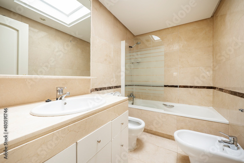 Conventional toilet with cream colored marble walls  recessed mirror and white sink