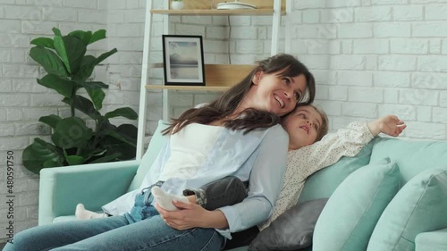 Mother tickling her daughter while they play together on the sofa, spending time at home.