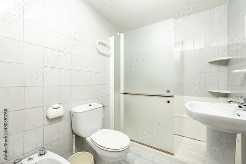 White bathroom with shower and glass partition, white porcelain sink and toilet