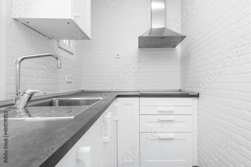 Vacation rental kitchen with white cabinets  white brick walls  gray countertop and stainless steel sink and range hood in the corner