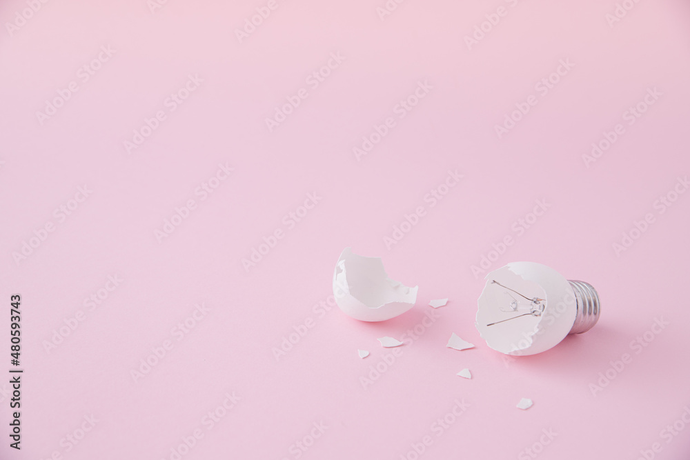 Egg lightbulb on pastel pink background with broken or shattered egg shell. Minimal concept. Easter inspiration. Flat lay. Broken idea. Lightbulb idea concept.