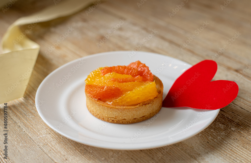 Tartlet - a dessert with tangerine and grapefruit lies on the table with a postcard for Valentine's Day Tartlet - a dessert with tangerine and grapefruit lies on the table with a postcard for Valentine's Day