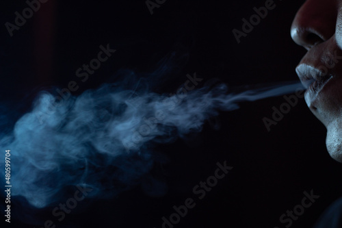 close up of a mouth blowing cigarette smoke in the dark