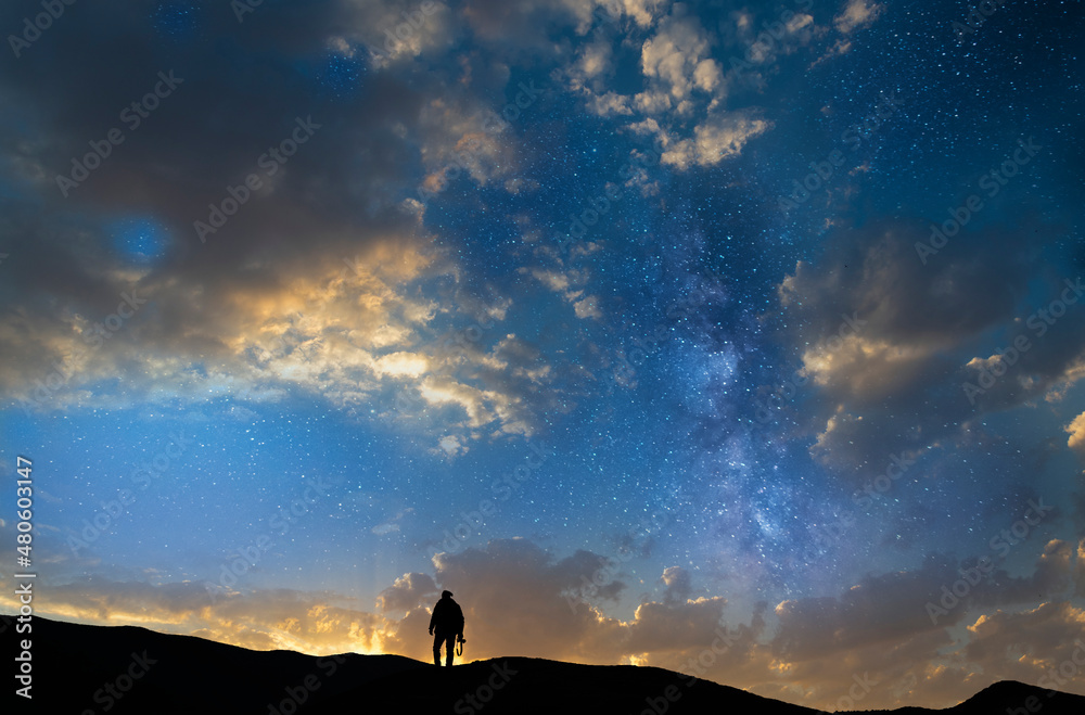 Silhouette of a person in the sunset and stars.  Photographer silhouette stands on the  hill with camera.