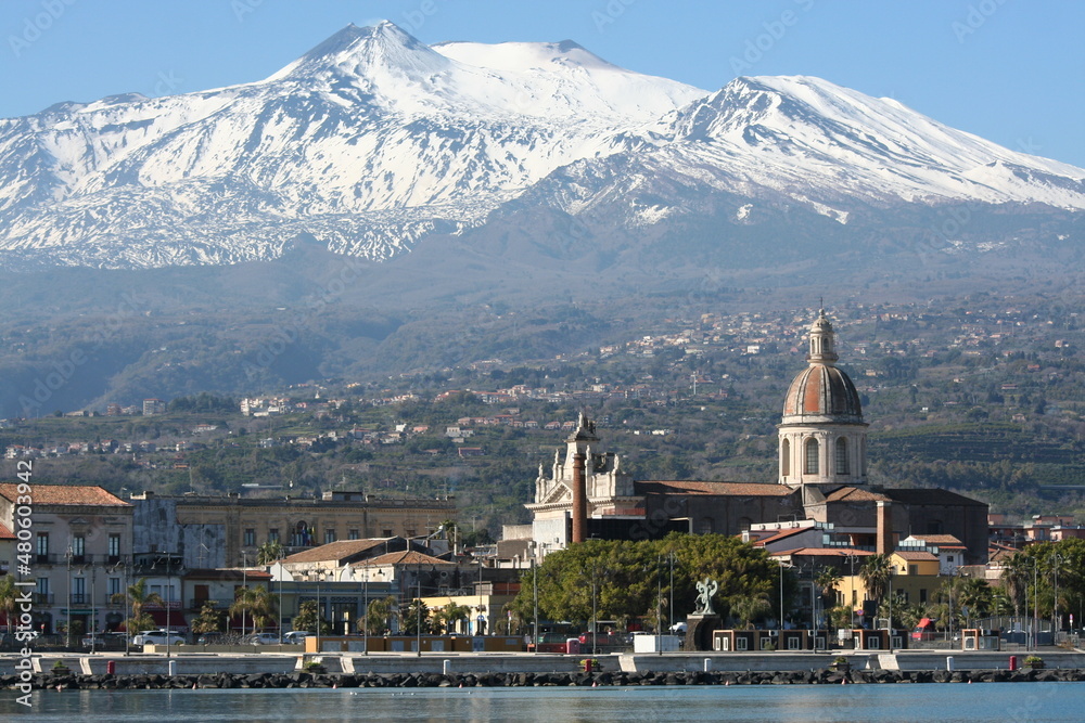 Foto panoramica del paese portuale di Riposto, con il mare in primo piano, il campanile e il vulcano etna sullo sfondo
