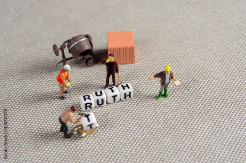 Fototapeta Naklejka Na Ścianę i Meble -  the team of miniature construction workers figurines seting up a word truth made of white cubes on grey background