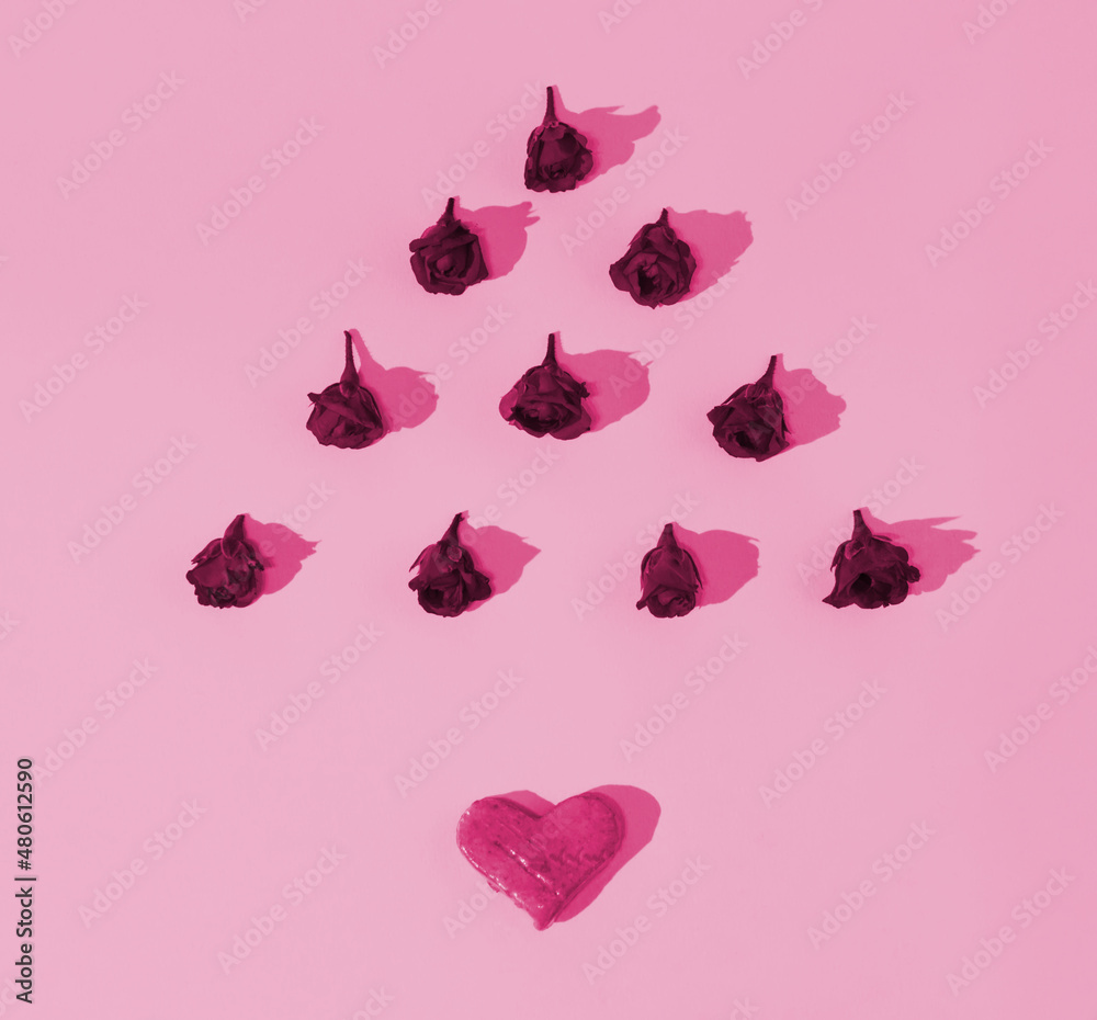 Fototapeta premium A geometrical floral pattern made of fresh rose buds in a shape of a triangle with a pink heart on pink background. Minimalist concept of love. Anniversary or Valentine’s pattern. Copy space. Flat lay