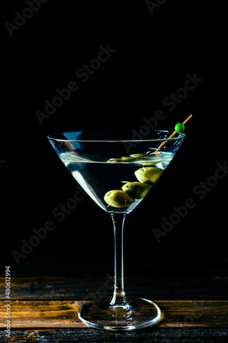 Elegant dry martini glass with sprinkled olives on black background with copy space. Vertical orientation.