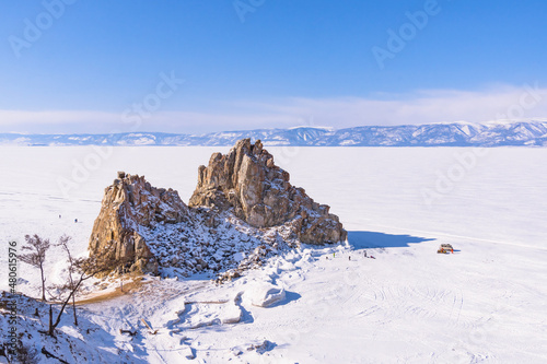 Sacred Shamanka Mountain on Olkhon Island in winter. View of the frozen Lake Baikal on a sunny day. View from above. Below, tourists walk on the ice