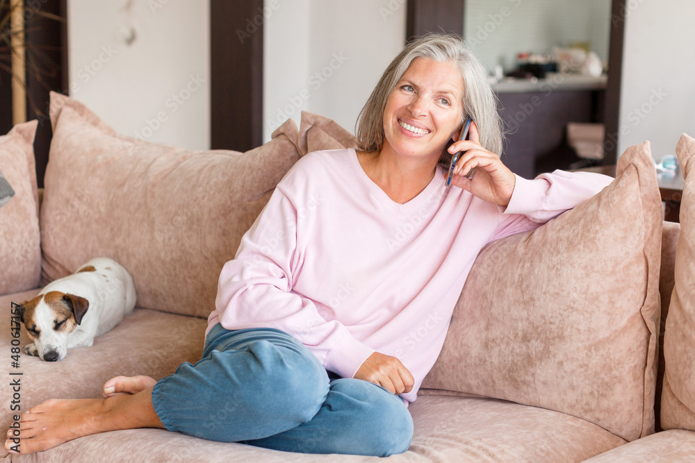 Pleased middle-aged white woman talking on mobile phone on couch