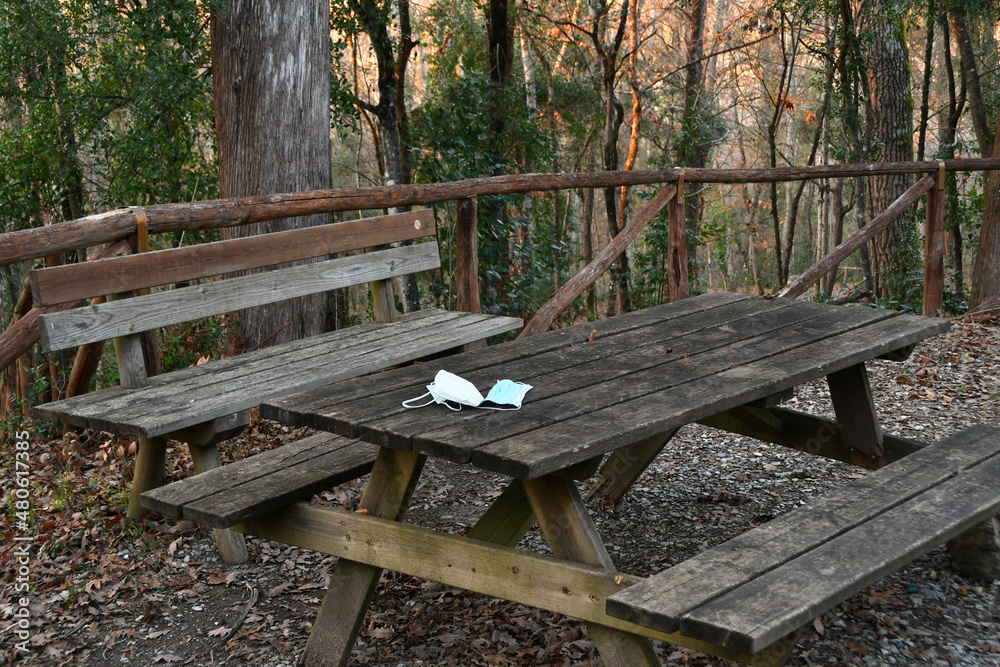 Used protective masks abandoned on on a park's wooden table. Used protective masks abandoned during the Coronavirus pandemic on public places.