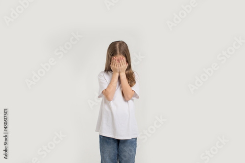 a young beautiful teenage girl is crying with her hands covering her face on a white isolated background.