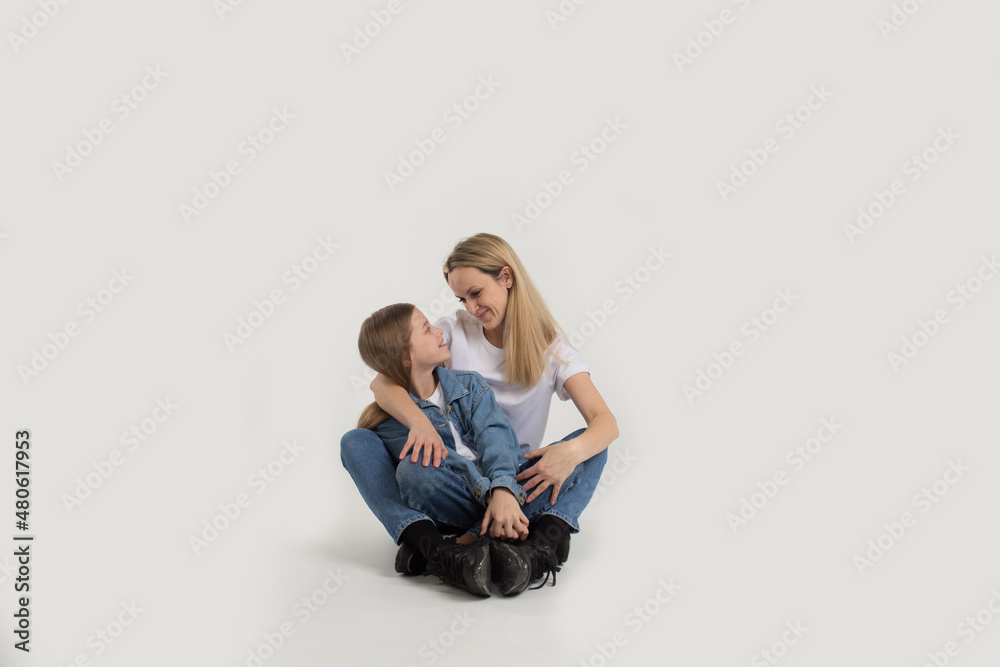 A beautiful young woman with her cute little daughter sitting on a white background. Mom and daughter are isolated. Softness