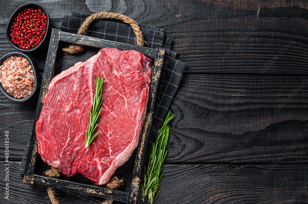 Beef raw fillet for steaks in a wooden tray with herbs. Black wooden background. Top view. Copy space