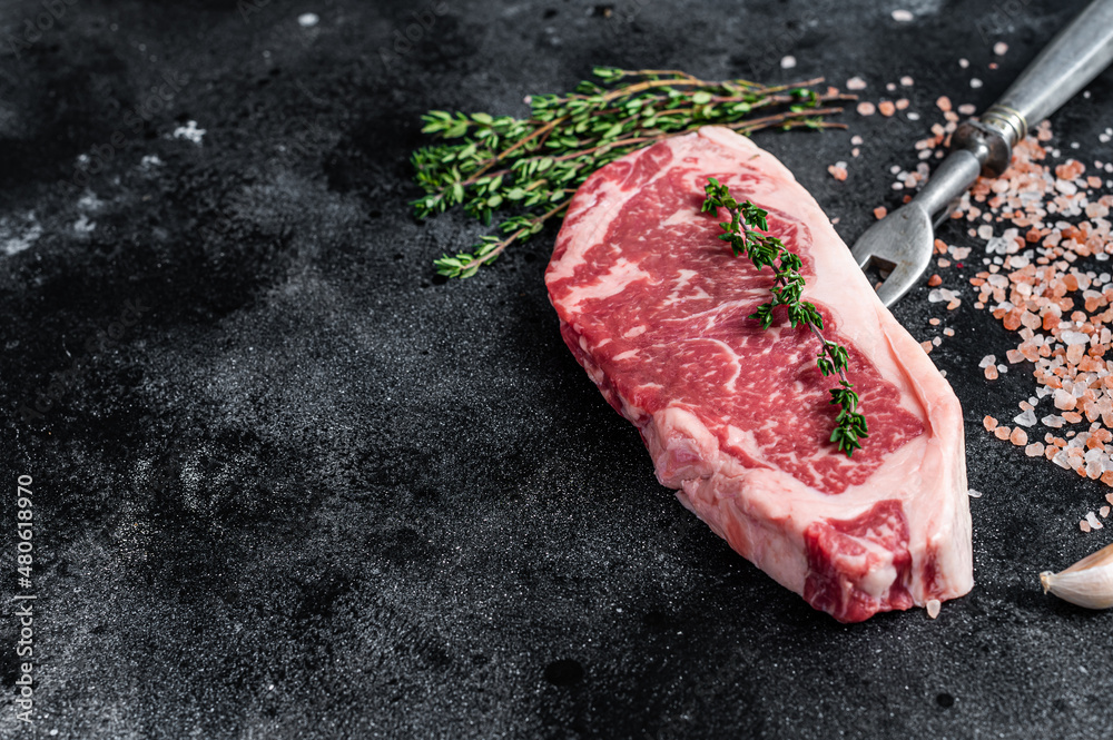 Raw striploin steak on a butcher table with salt and thyme. Black background. Top view. Copy space