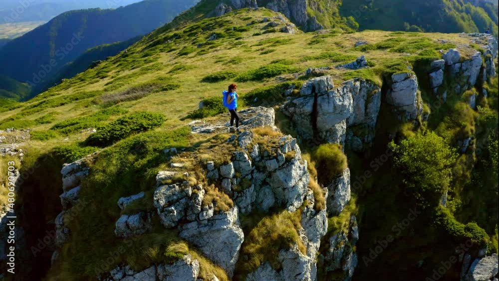 Aerial view of a woman on top of a mountain looking at the sunrise. Hiker girl celebrating scenic landscape enjoying nature vacation travel adventure. 4k