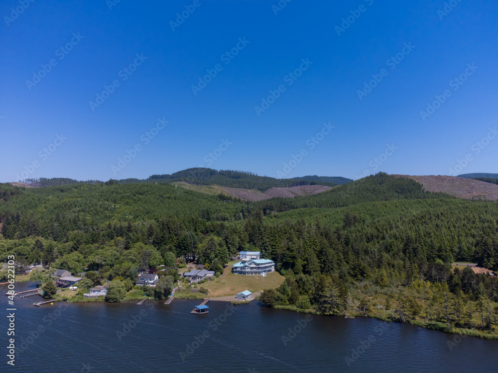 Nice panoramic shot. Dense green forest on the banks of the river, lake. On the shore are small lonely houses. Mountains are visible in the distance. Blue cloudless sky. calm scenes..