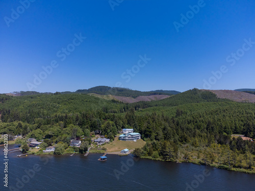 Nice panoramic shot. Dense green forest on the banks of the river, lake. On the shore are small lonely houses. Mountains are visible in the distance. Blue cloudless sky. calm scenes..