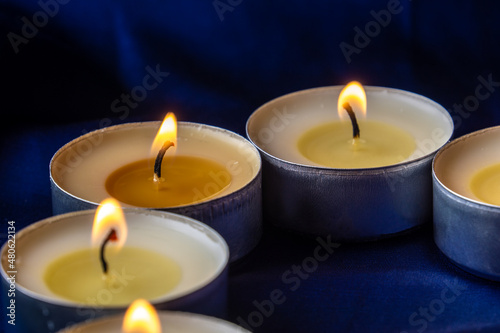 Round tea candles burn on a dark blue background. Wax melts in the candles.