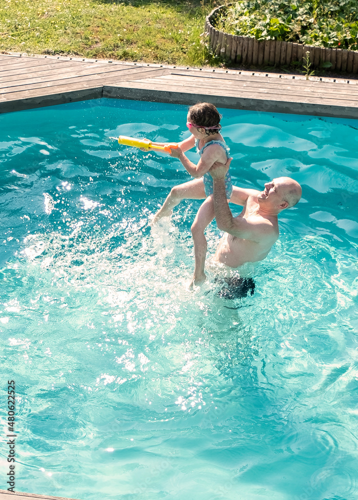 A middle-aged man and a 5-year-old Caucasian girl have fun swimming and splashing in an outdoor pool. Summer vacation in the backyard of the cottage.