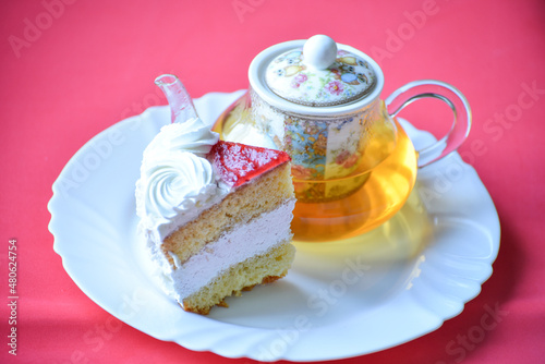 Green tea in teapot and peace of buscuit cake on pink background, tea ceremony. Sweets to eat and drink, birthday party set photo