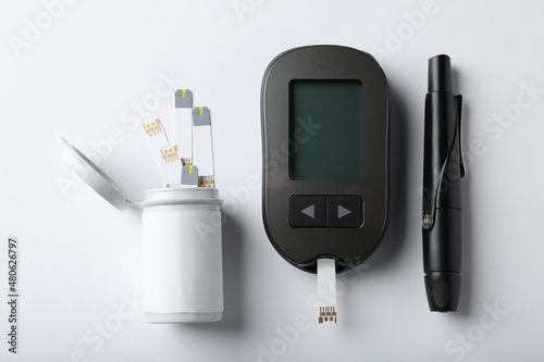 Digital glucometer, lancet pen and test strips on white background, flat lay. Diabetes control photo