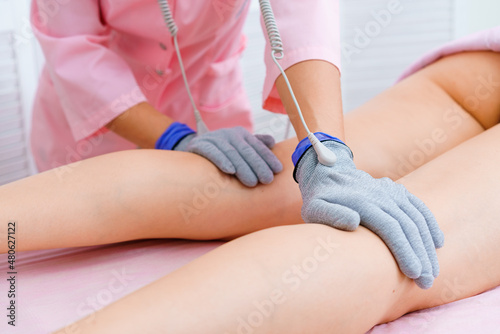 Masseuse makes an anti-cellulite massage on legs. Micro-sensory electric micro-current procedure bio ems for electrode stimulation of the face and body in conductive gloves. Anti-aging lifting