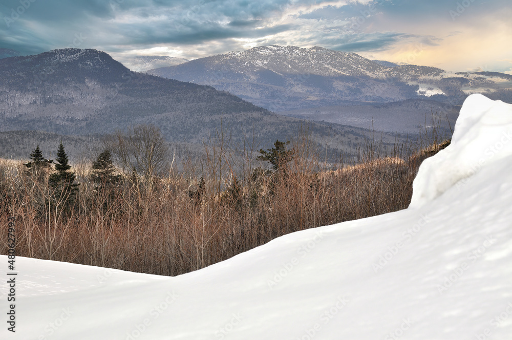 Chilly winter scene in White Mountain National Forest of New Hampshire. View of snow covered mountain peaks and colorful late afternoon sky from snowbank along scenic Kancamagus Highway.