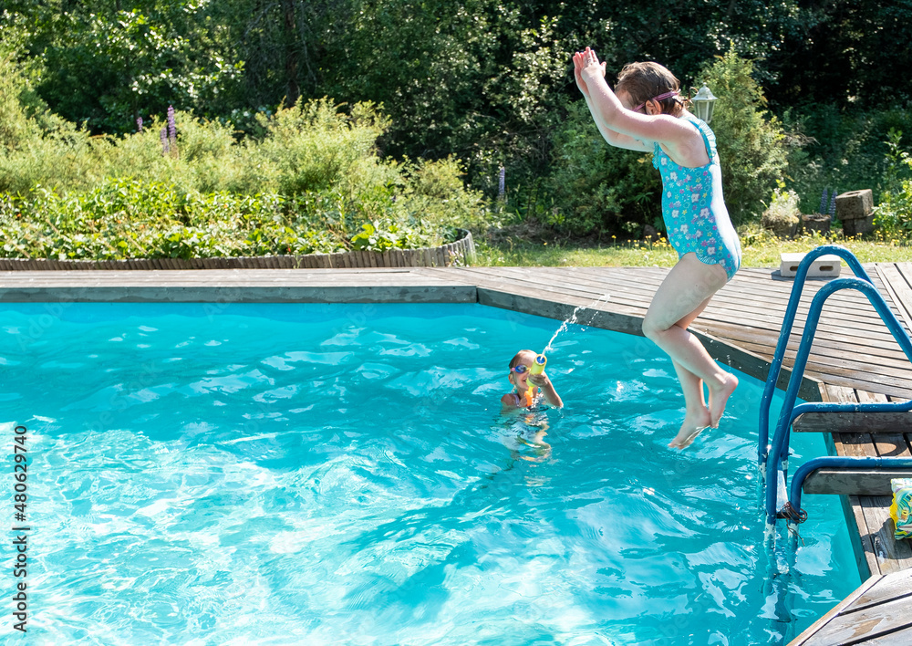 Caucasian girls 5 years old fun swims and jumps in the outdoor pool. Summer vacation in the backyard of the cottage.