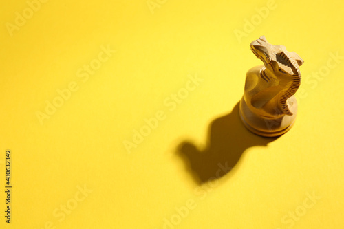 White wooden chess knight on yellow background, above view. Space for text