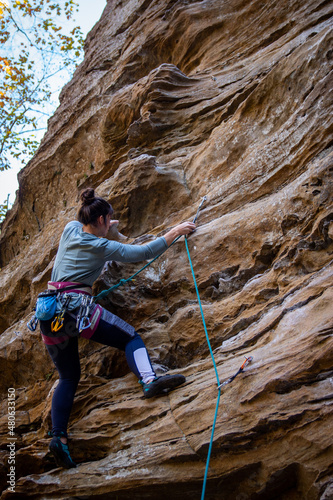 woman rock climbing clipping rope to quickdraw
