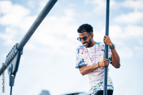 Smiling black man with sunglasses enjoying himself happily on the street attached to a bridge cable