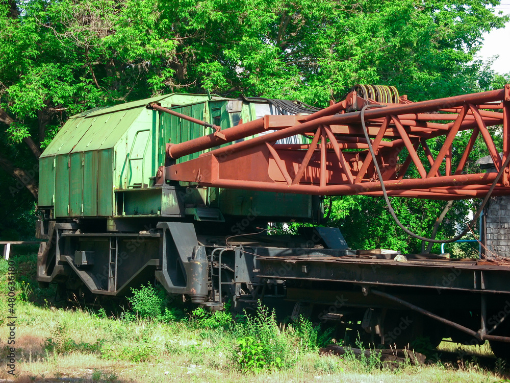 railway crane stands on abandoned tracks near trees 