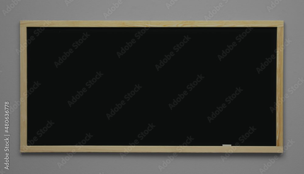 Clean black chalkboard hanging on grey wall Clean black chalkboard hanging on grey wall